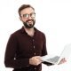 Portrait of a smiling handsome man in eyeglasses holding laptop computer and looking at camera isolated over white background